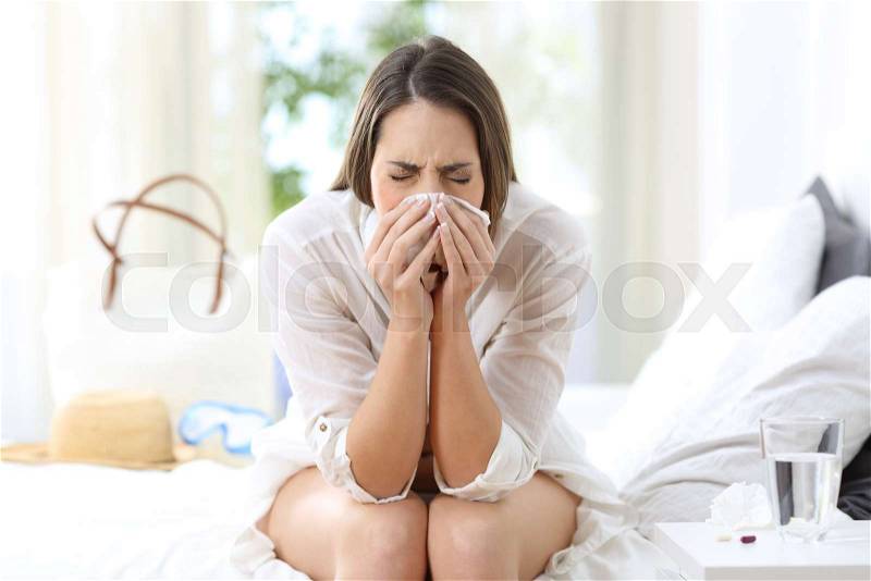 Ill woman coughing in an hotel room on summer vacations on the beach, stock photo