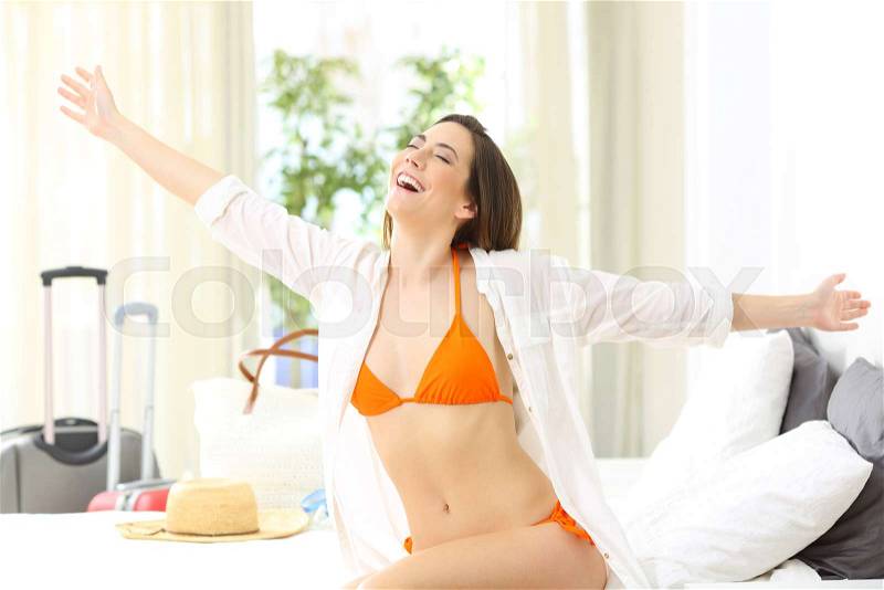 Excited lady wearing bikini celebrating arrival to an hotel room on summer vacations on the beach, stock photo