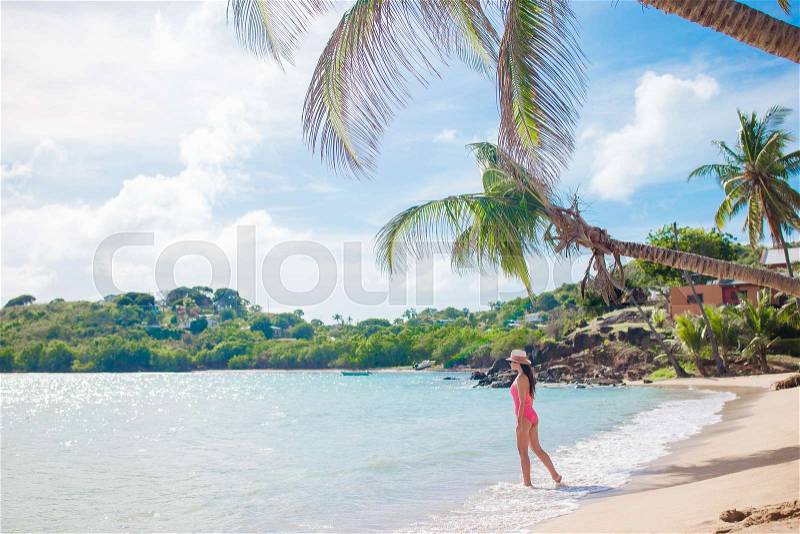 Young woman in bikini and straw hat on tropical beach. Beautiful girl under the palm tree on tropical Carlisle bay beach with white sand and turquoise ocean water at Antigua island in Caribbean, stock photo