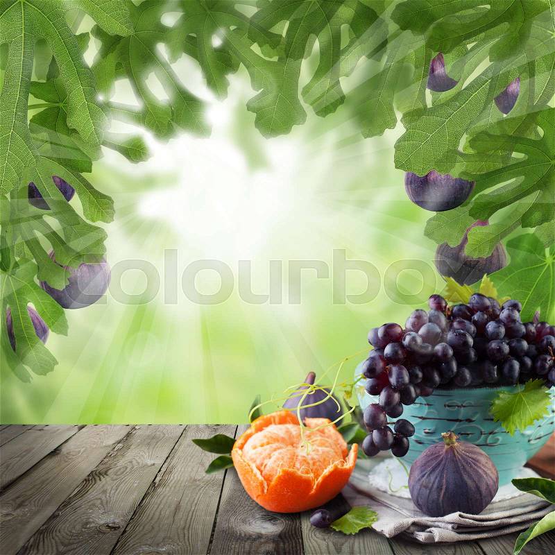 Mandarin, figs and grapes fruits on abstract green bokeh background with green leaves and empty wooden table with copy space. Summer food background, stock photo