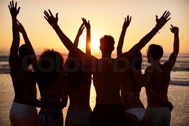 Silhouette Of Friends On Beach Vacation Watching Sunset Over Sea, stock photo