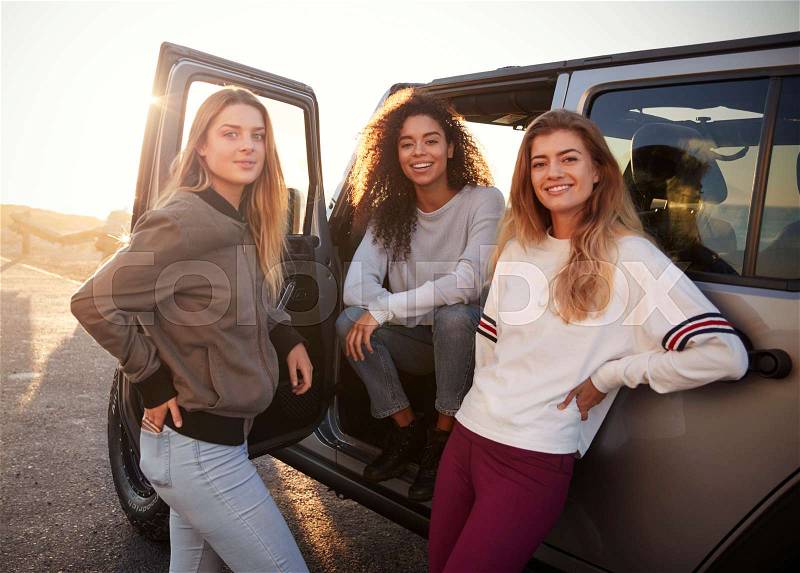 Three female friends on road trip looking at camera from car, stock photo