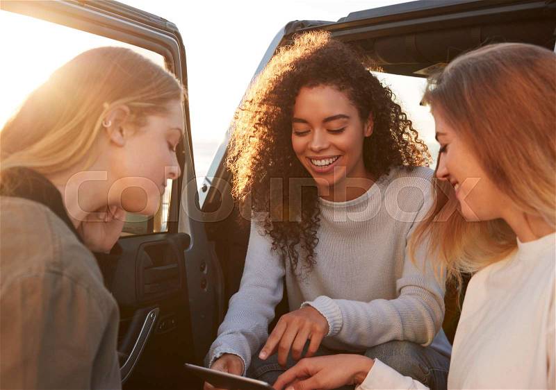 Female friends planning road trip route with tablet computer, stock photo