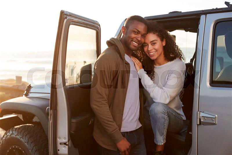 Young mixed race couple on a road trip embracing by car, stock photo