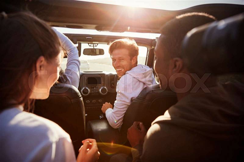 Four young adult friends together in a car on a road trip, stock photo