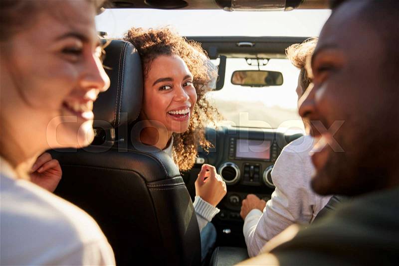 Four young adult friends in a car on a road trip together, stock photo