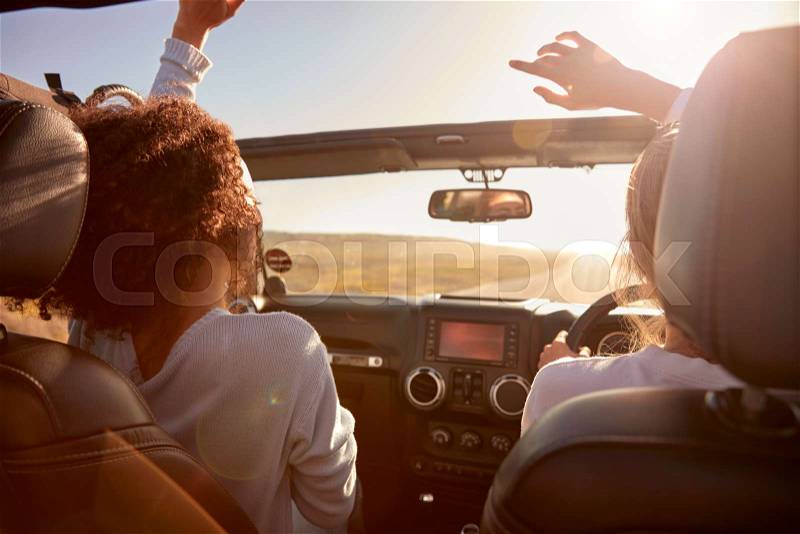 Young adult girlfriends driving with sunroof open, back view, stock photo