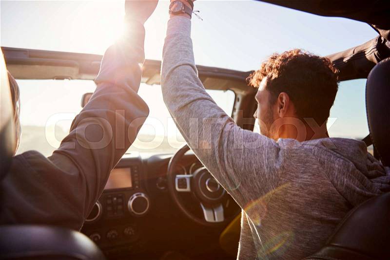 Young couple driving with sunroof open and hands in the air, stock photo