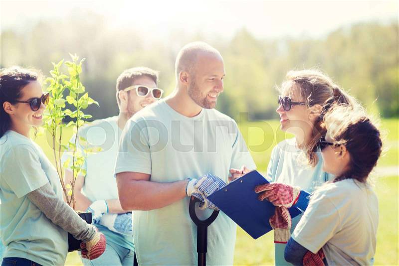 Volunteering, charity, people and ecology concept - group of volunteers with clipboard planting trees in park, stock photo
