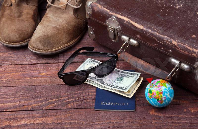 Travel concept with Vintage suitcase, sunglasses, old camera, suede boots, case for money and passport on wooden floor, stock photo