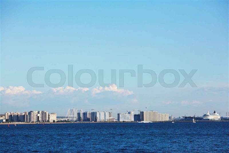 Blue waves of sea and bright sky with cityscape on horizon on hot summer day, stock photo
