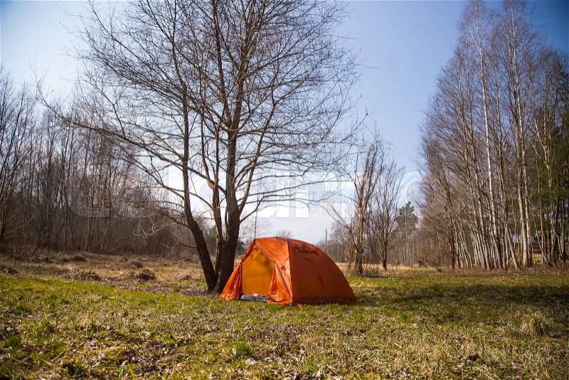 An orange tent built on the bank of the river. Hiking camp in the spring. Early spring scenery, stock photo
