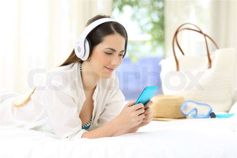 Hotel guest lying on a bed listening to music on summer vacations, stock photo