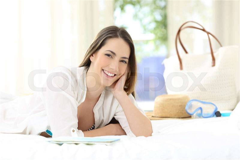 Satisfied hotel guest looking at camera lying on a bed in a room, stock photo