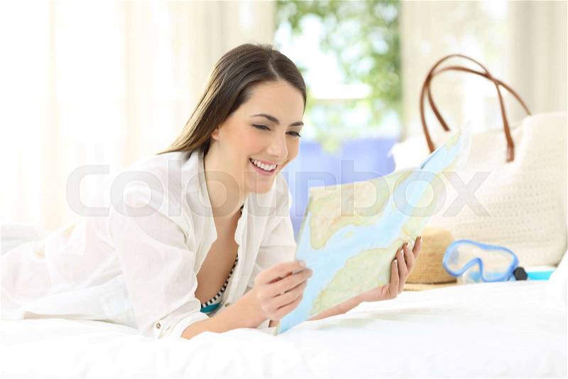 Happy tourist planning summer vacations lying on a bed in an hotel room, stock photo
