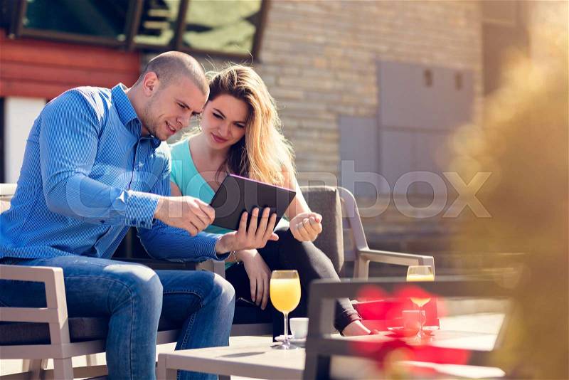 Young couple, woman and man, in street cafe drinking coffee and juice while watching pictures of holidays, stock photo