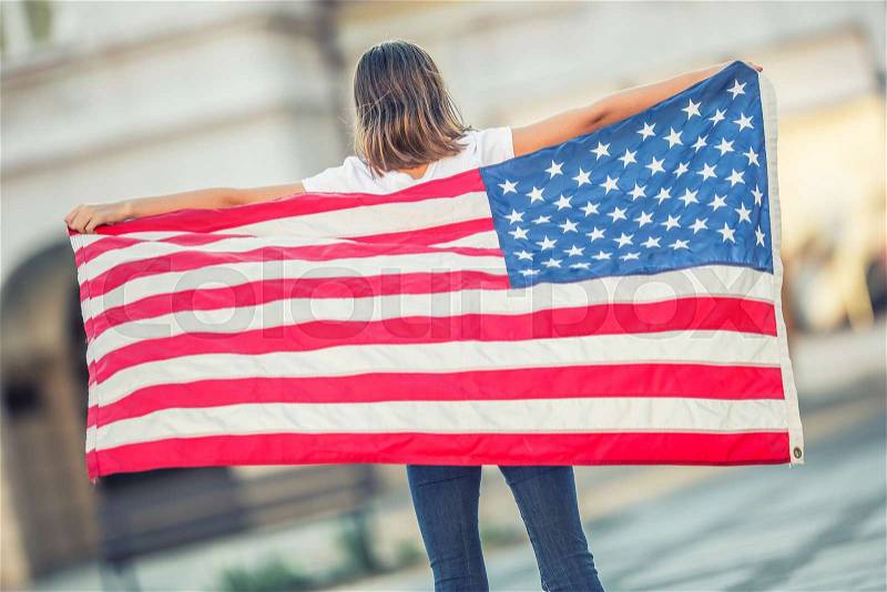 Happy young american school girl holding and waving in the city with USA flag. , stock photo