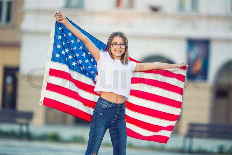 Happy young american school girl holding and waving in the city with USA flag. , stock photo