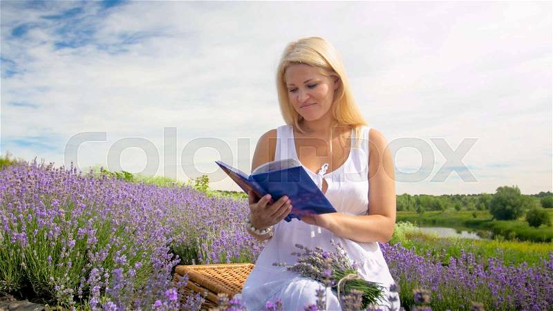 Portrait of young blonde woman reading book in lavender field at morning, stock photo