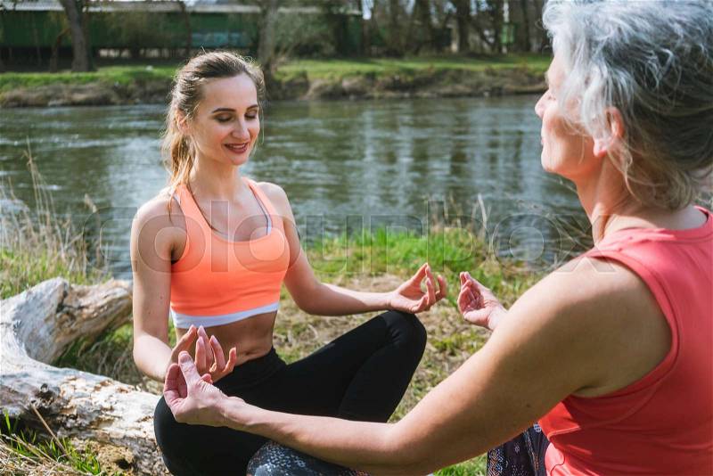 Old and young woman doing yoga on log by the river meditating , stock photo