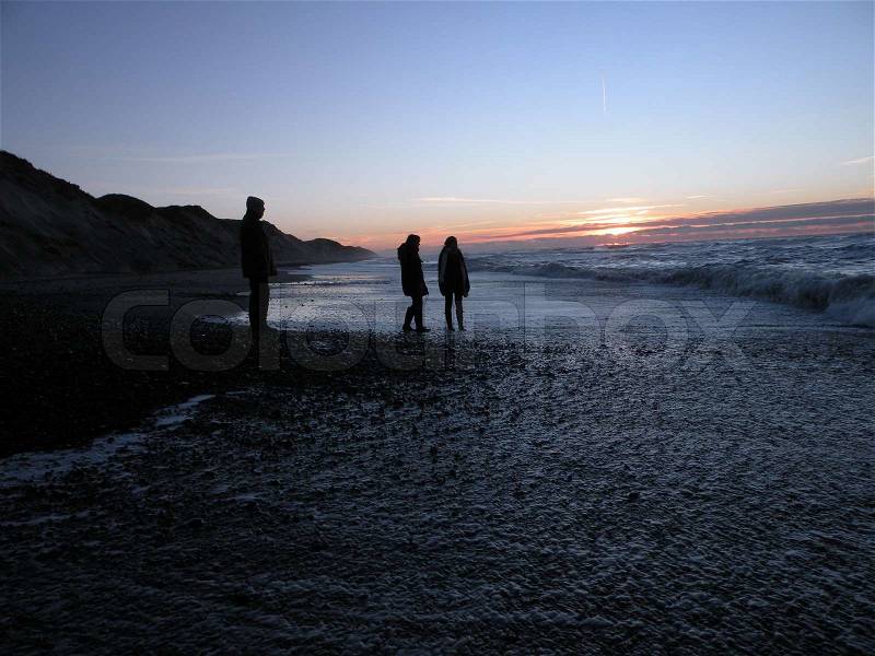 Silhouette of three people in sunset on beach at north sea, Thy National Park, Jutland, Denmark, stock photo