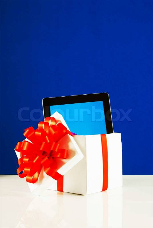 Tablet PC in a gift box against blue background, stock photo