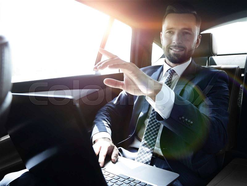 Businessman sitting in the back seat in the car and pointing his finger forward, stock photo