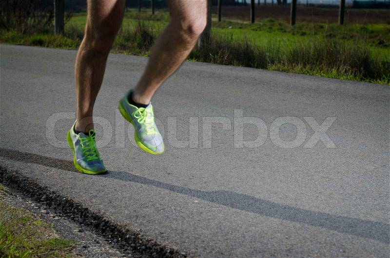 Running sport shoes outdoors in action on country road Male shoes on young man training Slight motion blur, focus on back running shoe, stock photo
