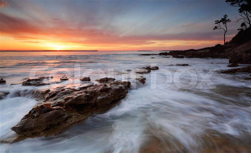 Beautifuol sunrise over the bay as the ocean ebbs and flows gently over rocks at the shore edge, stock photo