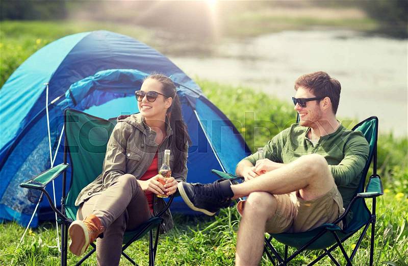 Camping, travel, tourism, hike and people concept - happy couple drinking beer or cider at campsite tent, stock photo