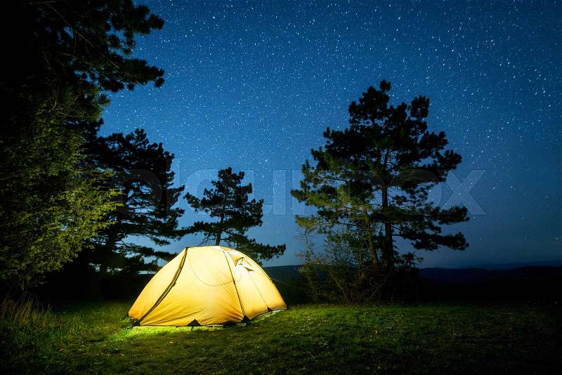 Glowing camping tent in the night mountain forest under a starry sky, stock photo