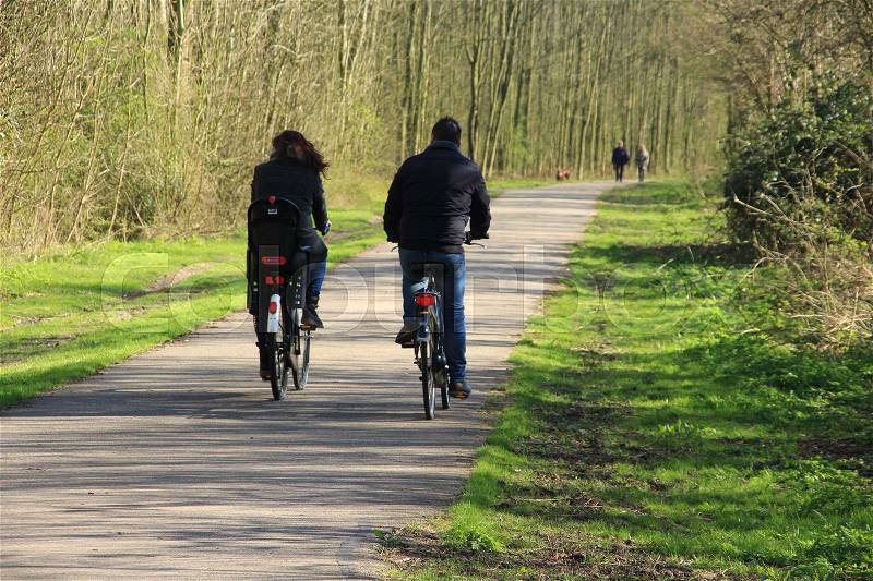 Couple, man and wife are biking and in the distance a walking couple with the dog in the park in the village Simonshaven in spring, stock photo