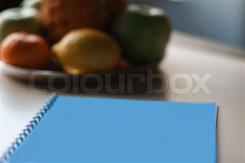 Close-up recipe notebook on the kitchen table at home. Apples, fruits blured on background, stock photo