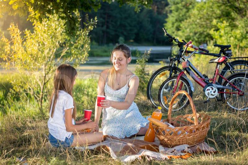 Happy young family sitting on blanket under tree and having picnic, stock photo