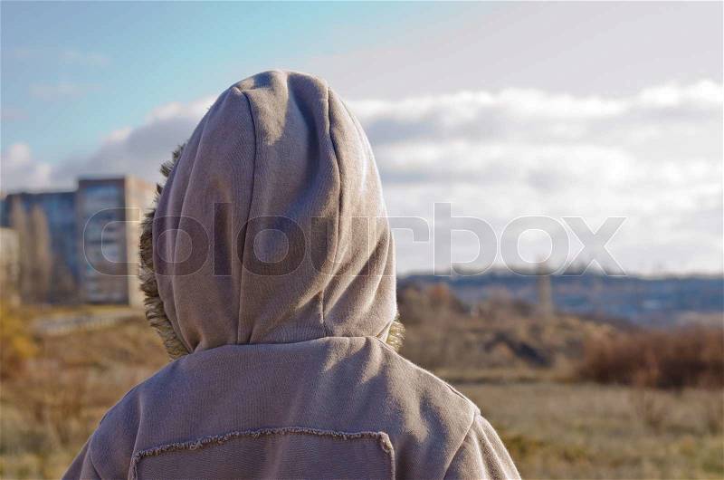 The little boy in a jacket costs a back on the nature in the autumn and looks at a city in the distance, stock photo