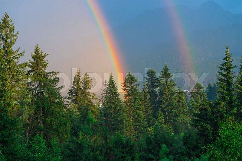 A beautiful natural phenomenon, two rainbows against the backdrop of mountains covered with forest after rain, stock photo
