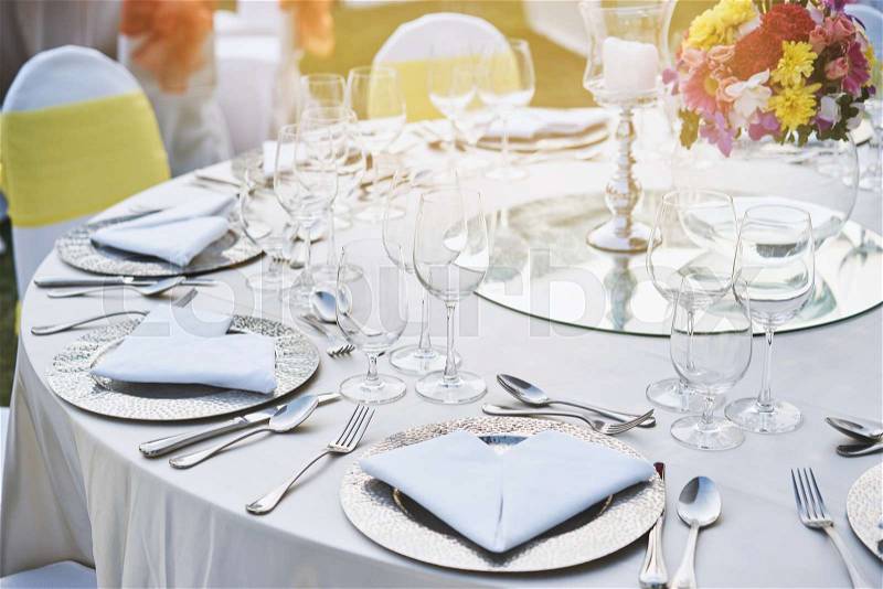 The closeup shot of wedding reception dinner table setup with the empty glasses of wine and water, stainless plate, spoon, fork and napkin, The candle and flowers use for decoration, stock photo