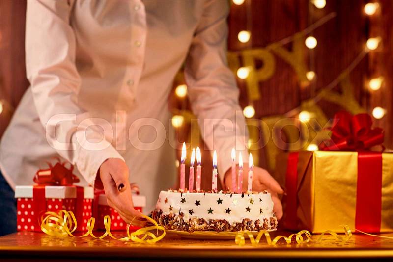 Cake Happy Birthday with candles and hand of the girl on background garlands and boxes gifts, stock photo