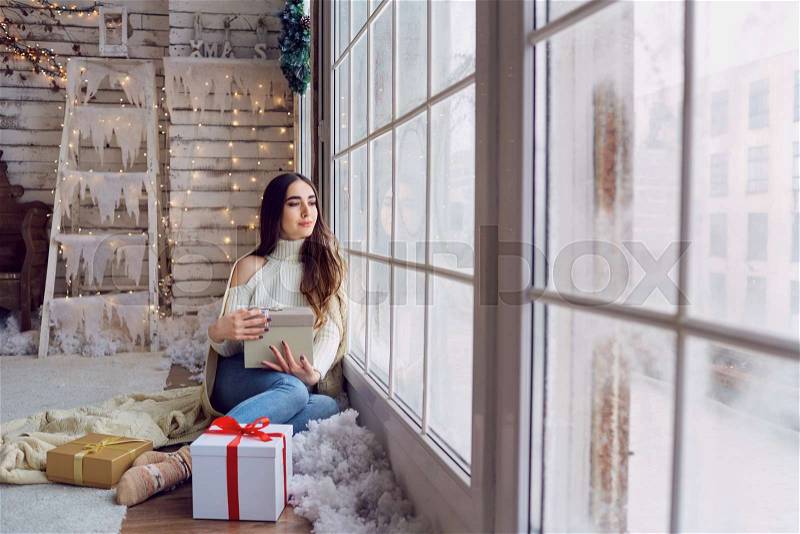 The girl at the window with gifts in the winter. A young woman looks out the window at Christmas, stock photo