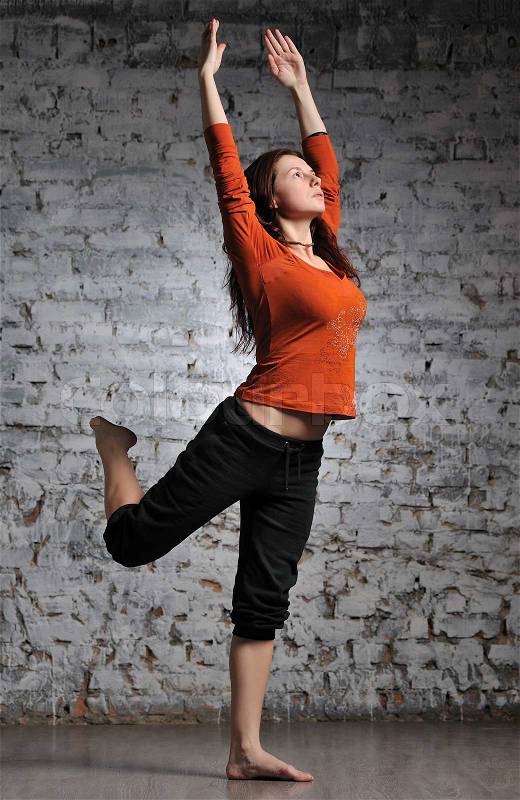 Full-length portrait of young beautiful woman doing yoga excercise against a brick wall, stock photo