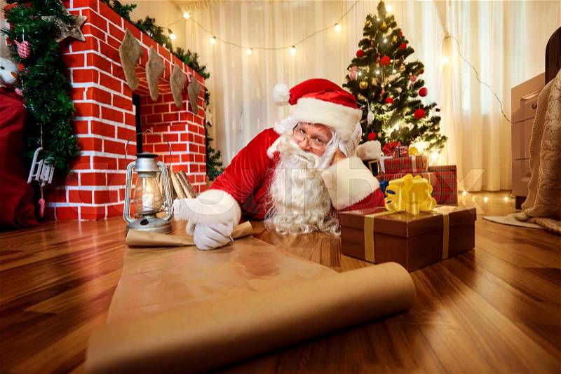 Santa Claus at Christmas, New Year\'s Eve wrote a list of gifts to children on paper in the room with the Christmas tree and fireplace, stock photo