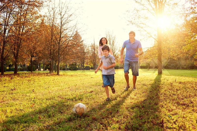 Happy family playing in nature late afternoon sunlight in the fall, summer. Mother, father and son playing with a ball on the grass in the park, laughing and smiling, fun, joy, stock photo