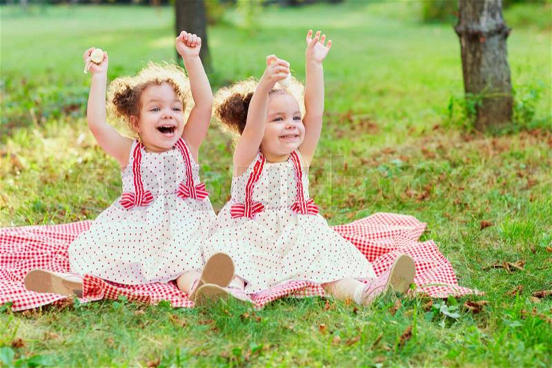 Happy twin sisters children. Girls sister in a park at a picnic laugh, smile, cry, have fun in the rays of the evening sun, stock photo