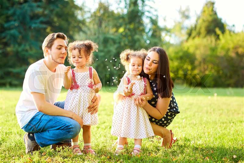 Happy family in the park outdoors in summer, autumn. Mother, father and daughter spending time together on the grass in the park.Parents with children blowing dandelions, stock photo