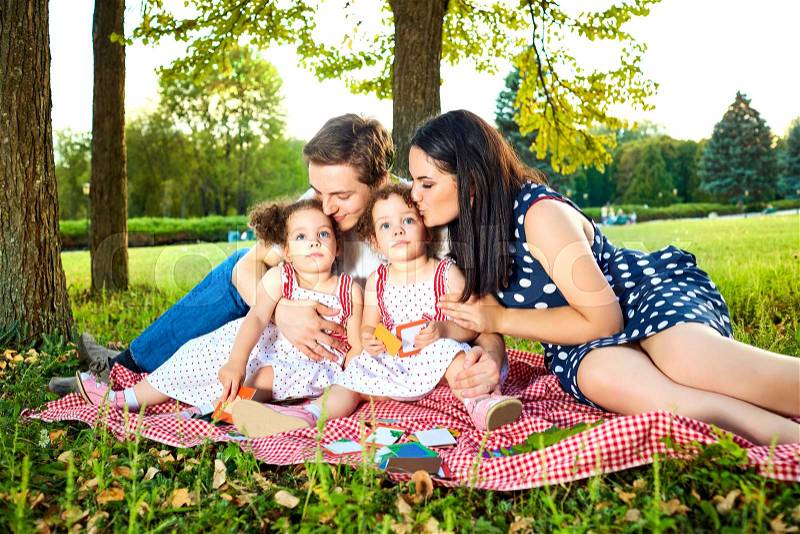 Happy family in the park summer, autumn. Parents and two daughters sitting, playing on the grass in nature. Mom and dad kiss their children happy. The concept of a happy family, stock photo