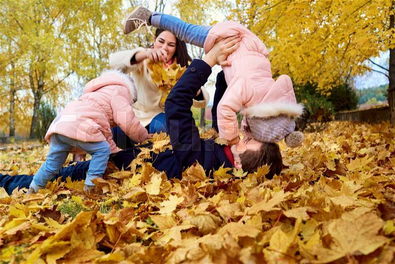 Happy family lying on the yellow leaves in the park playing actively in the autumn, fooling around, having fun. The concept of a happy family, stock photo