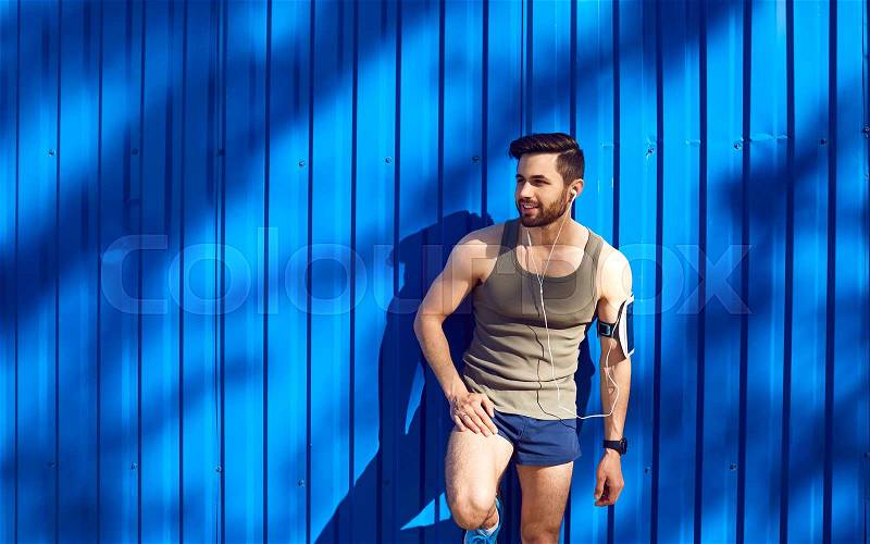 A man with a beard athlete runner in headphones against a blue wall background with space for text, stock photo