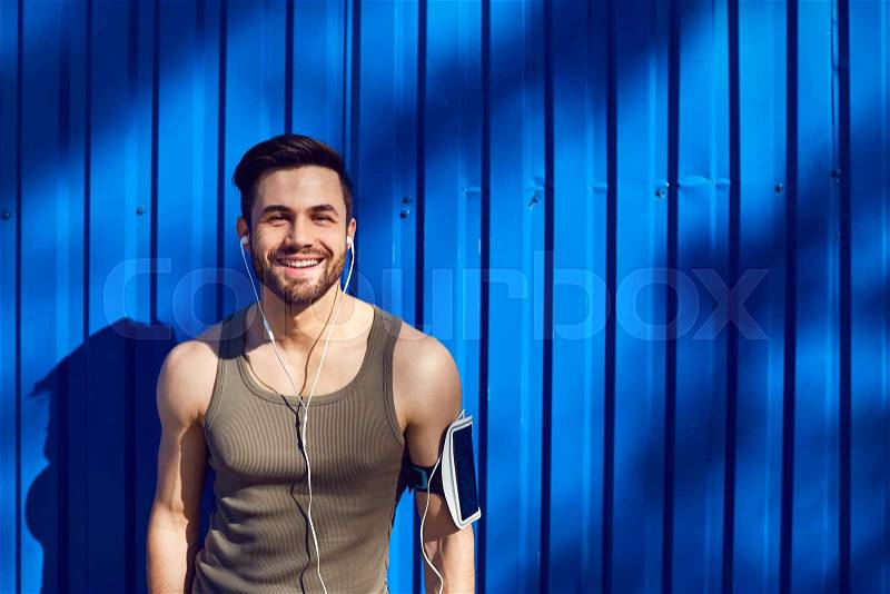 A man with a beard athlete runner in headphones against a blue wall background with space for text, stock photo