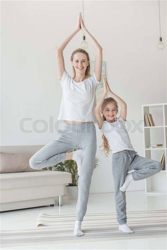 Happy mother and daughter balancing in tree pose together, stock photo