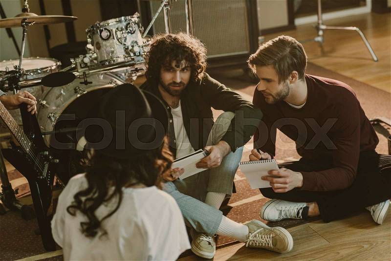 Young band writing music together while sitting on floor, stock photo